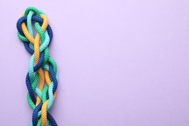 Photo of Braided colorful ropes on lilac background, top view with space for text. Unity concept