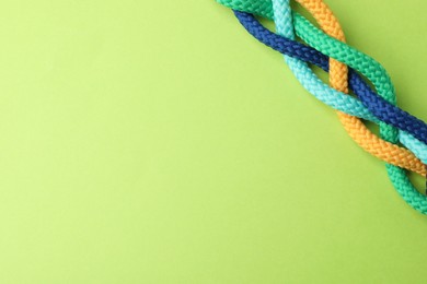 Photo of Braided colorful ropes on light green background, top view with space for text. Unity concept