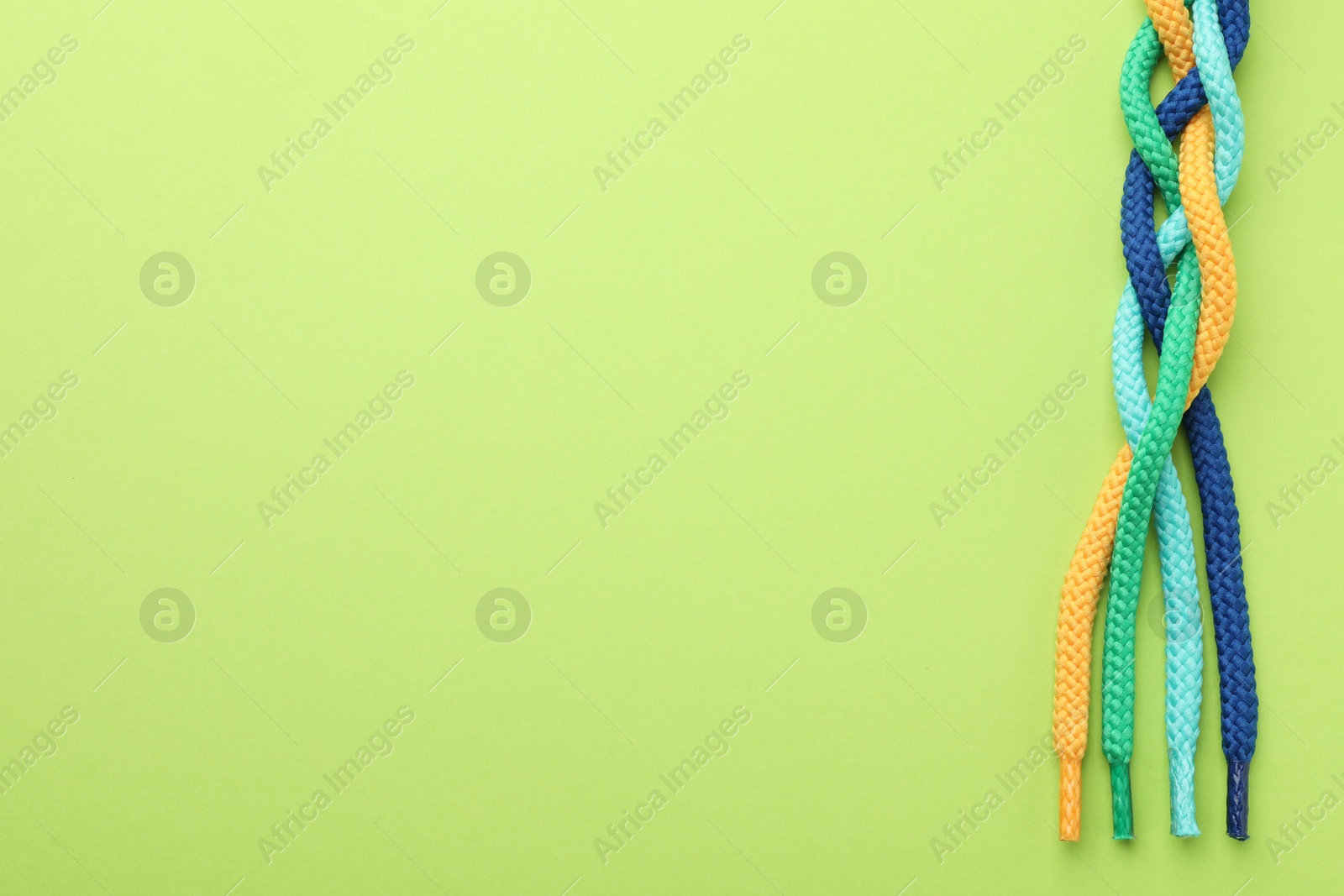 Photo of Braided colorful ropes on light green background, top view with space for text. Unity concept