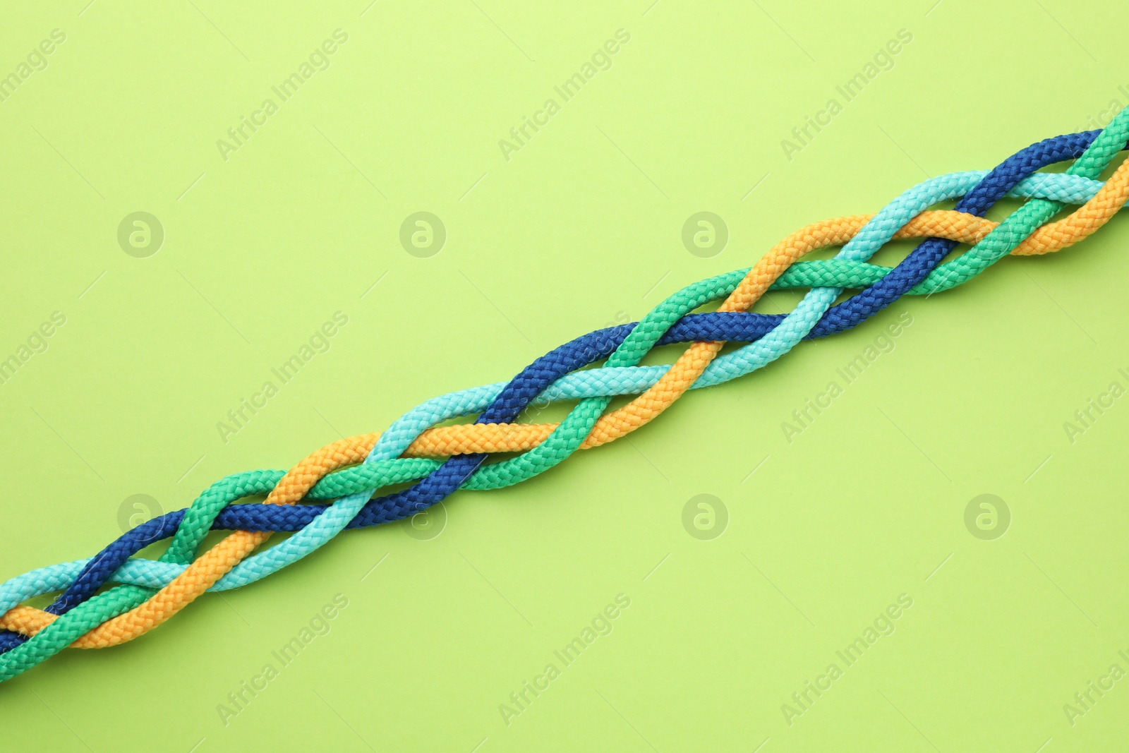 Photo of Braided colorful ropes on light green background, top view. Unity concept