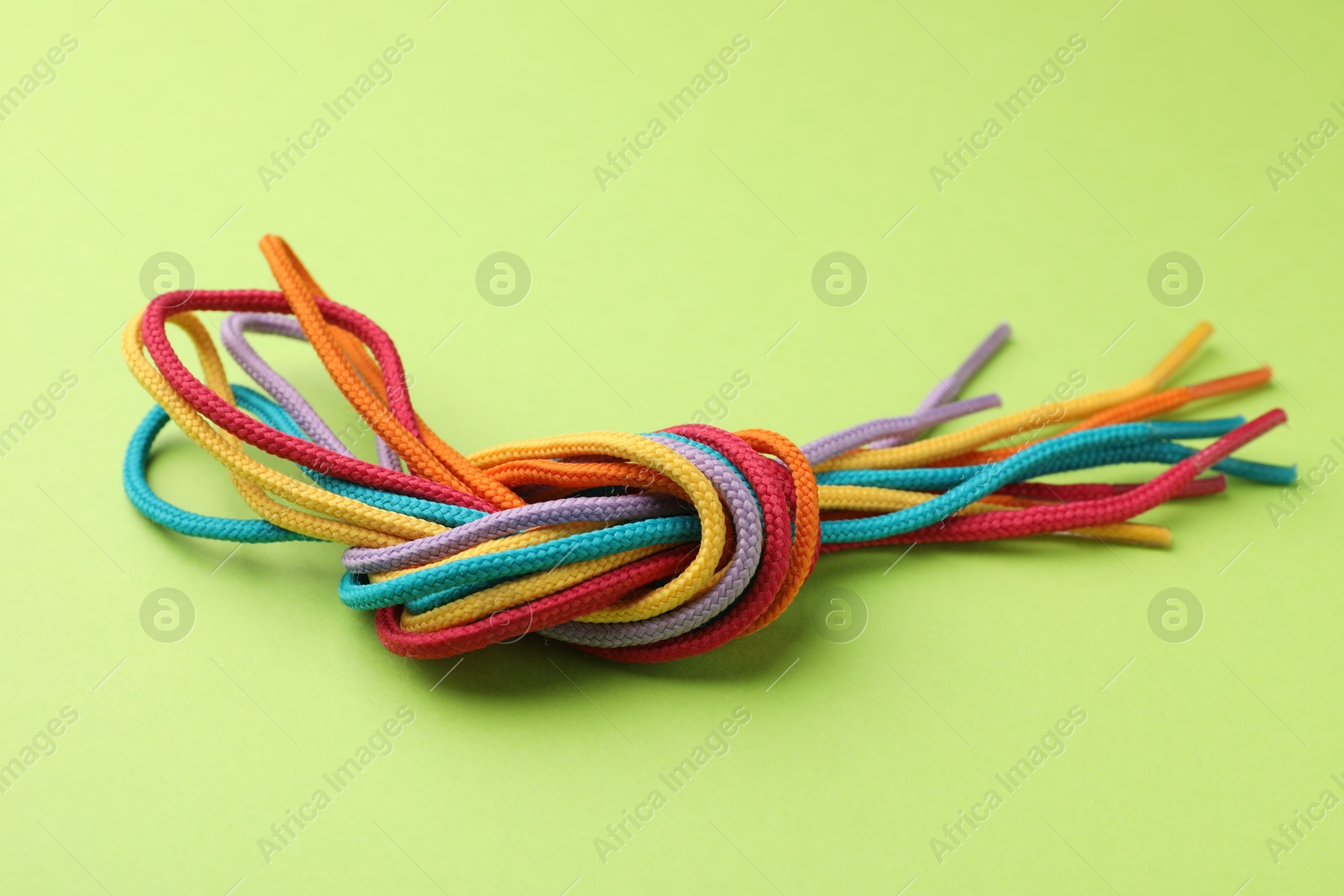 Photo of Colorful ropes tied in knot on light green background, closeup. Unity concept