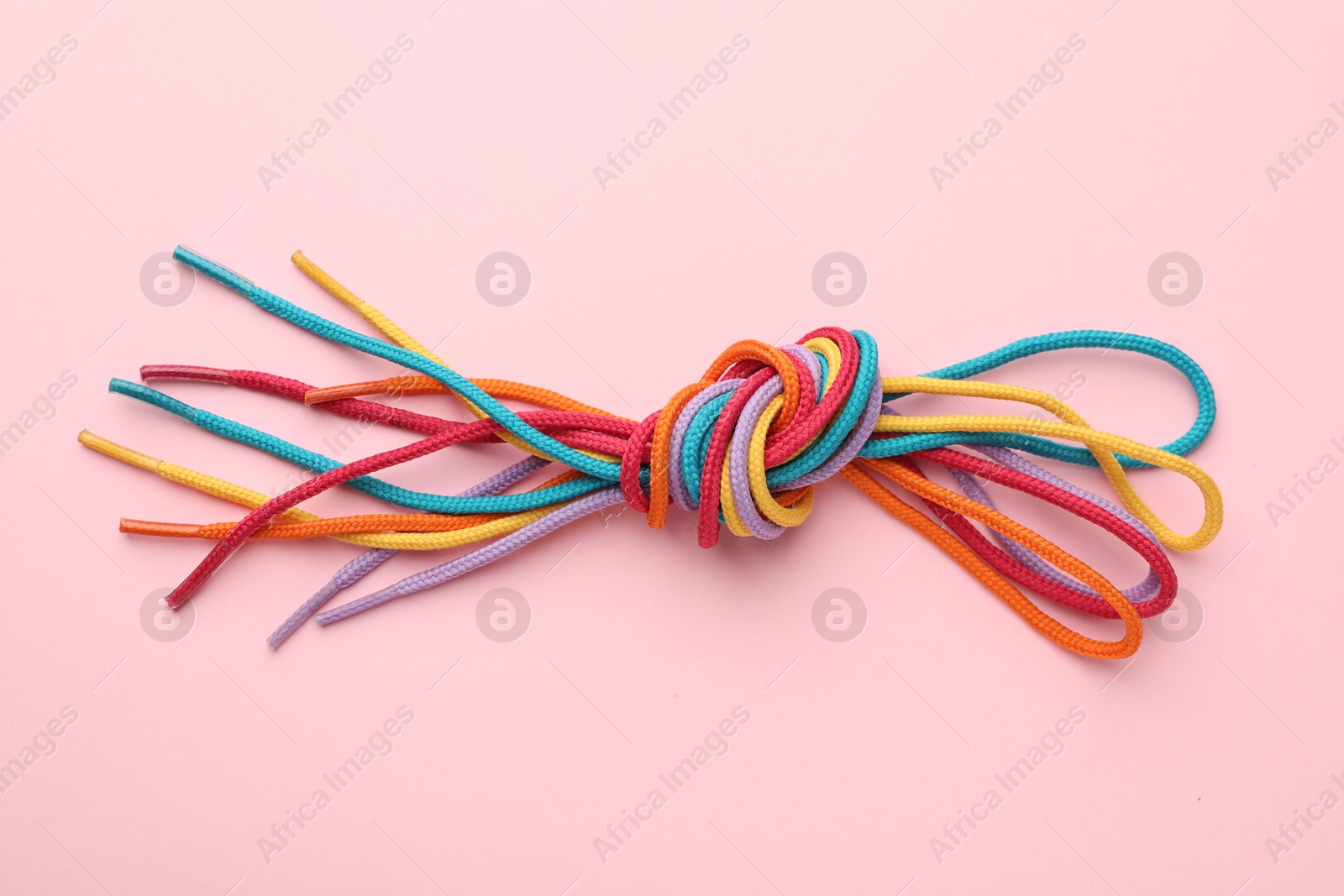 Photo of Colorful ropes tied in knot on light pink background, top view. Unity concept