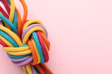 Photo of Colorful ropes tied in knot on light pink background, closeup with space for text. Unity concept