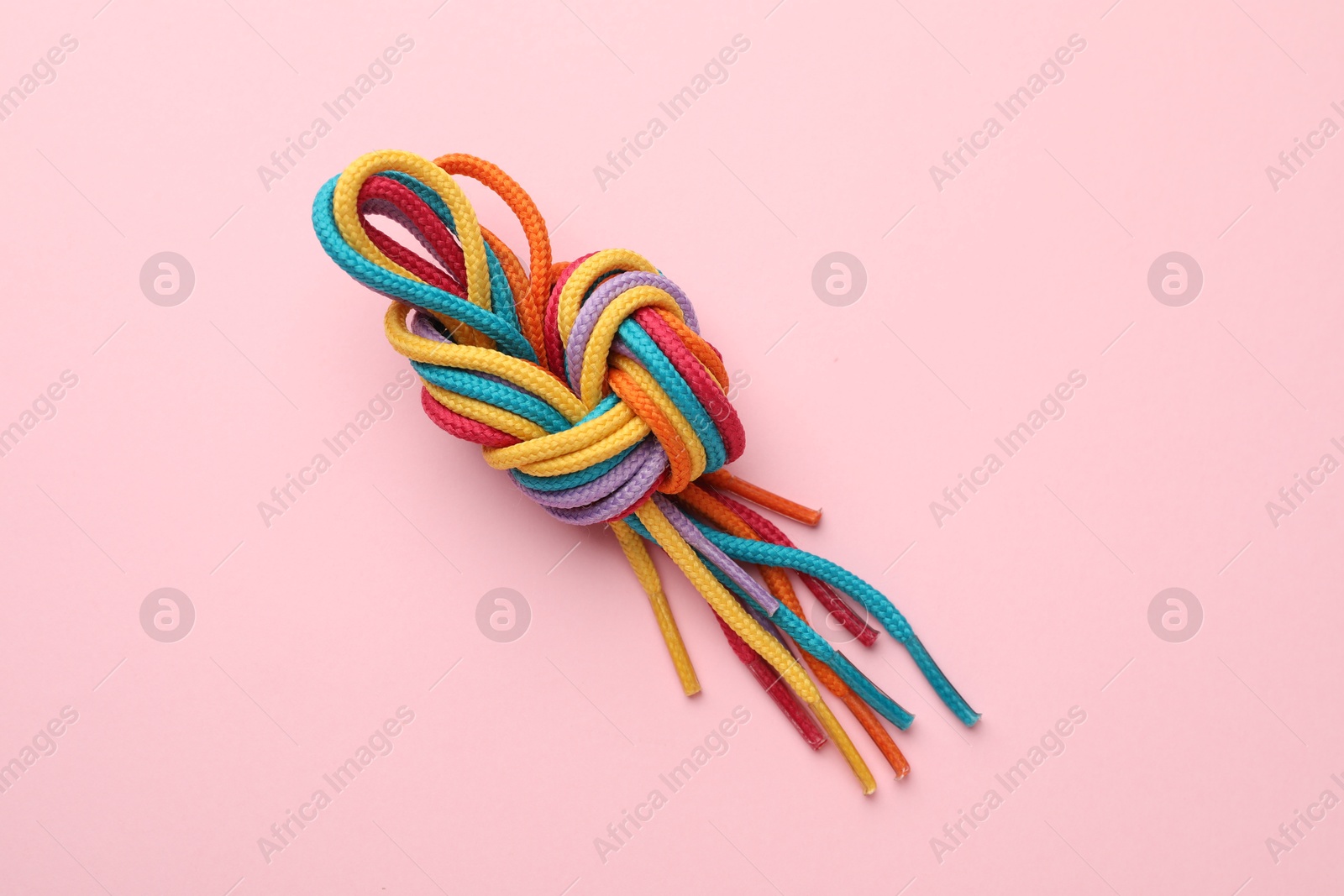 Photo of Colorful ropes tied in knot on light pink background, top view. Unity concept