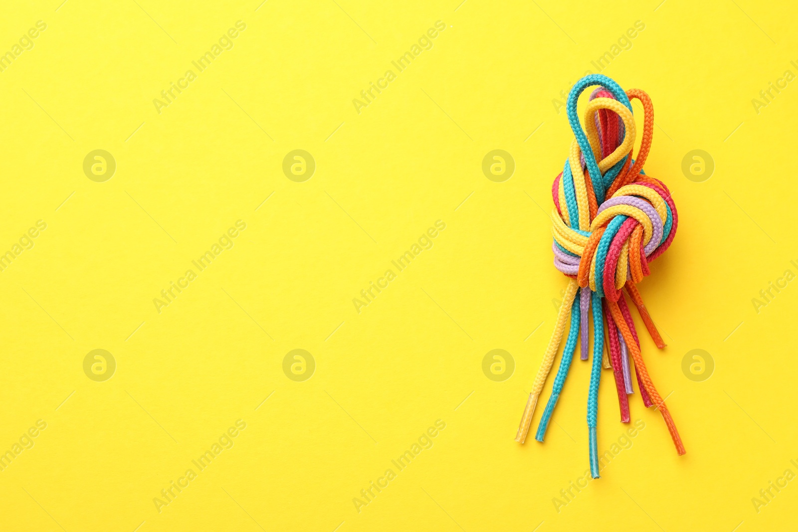 Photo of Colorful ropes tied in knot on yellow background, top view with space for text. Unity concept