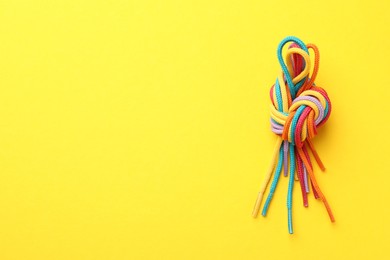 Photo of Colorful ropes tied in knot on yellow background, top view with space for text. Unity concept