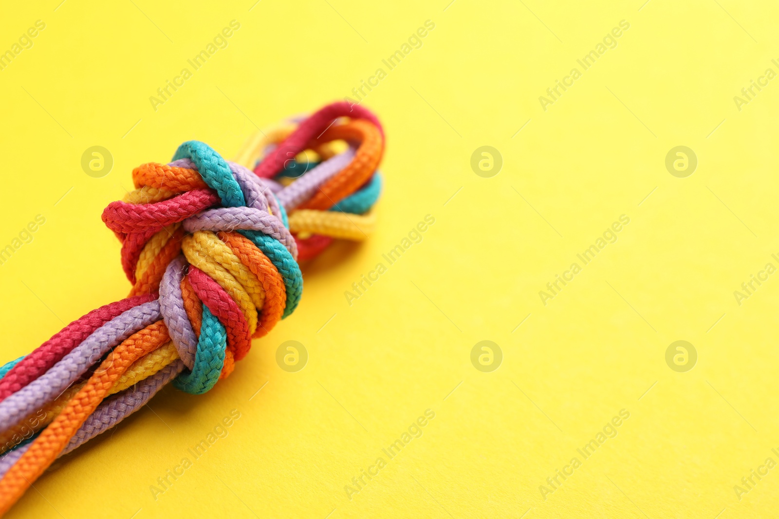 Photo of Colorful ropes tied in knot on yellow background, closeup with space for text. Unity concept