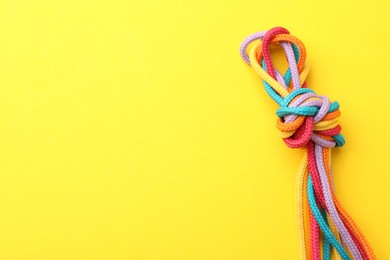 Photo of Colorful ropes tied in knot on yellow background, top view with space for text. Unity concept