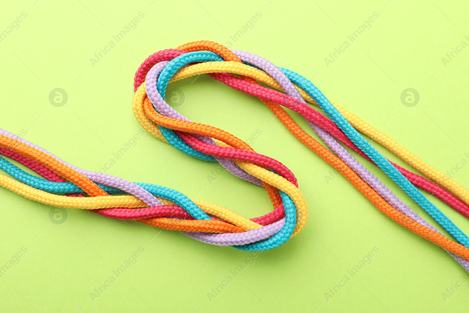 Photo of Braided colorful ropes on light green background, top view. Unity concept