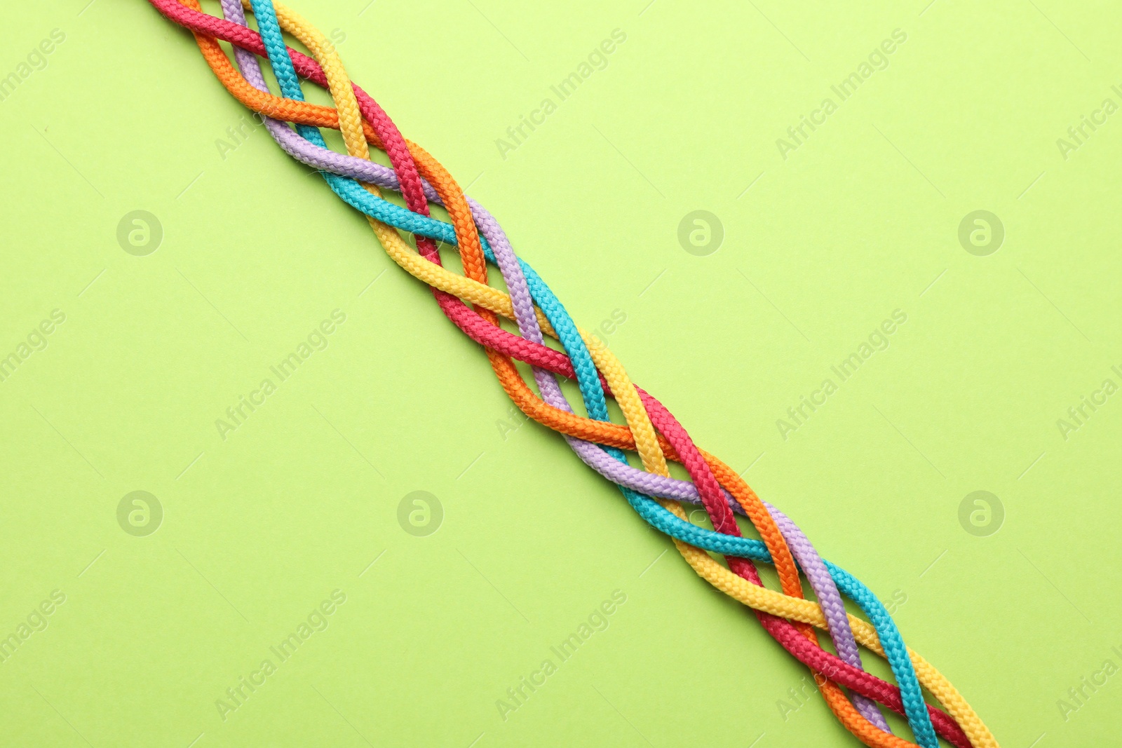 Photo of Braided colorful ropes on light green background, top view. Unity concept