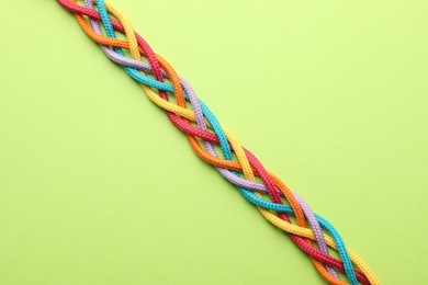 Photo of Braided colorful ropes on light green background, top view. Unity concept