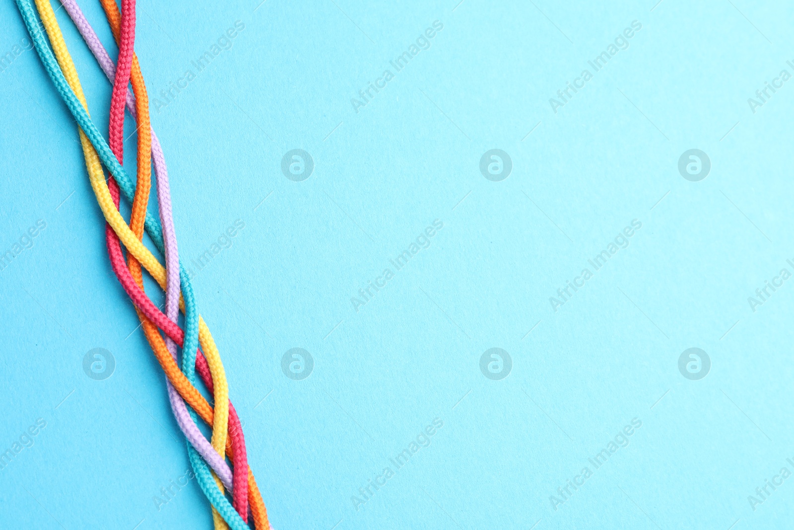 Photo of Braided colorful ropes on light blue background, top view with space for text. Unity concept