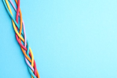 Photo of Braided colorful ropes on light blue background, top view with space for text. Unity concept