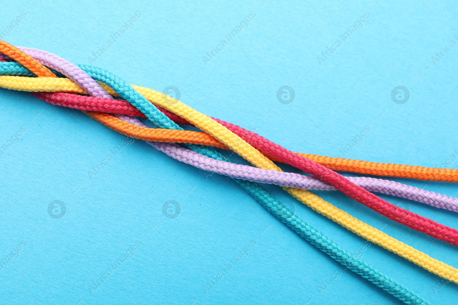 Photo of Braided colorful ropes on light blue background, top view. Unity concept