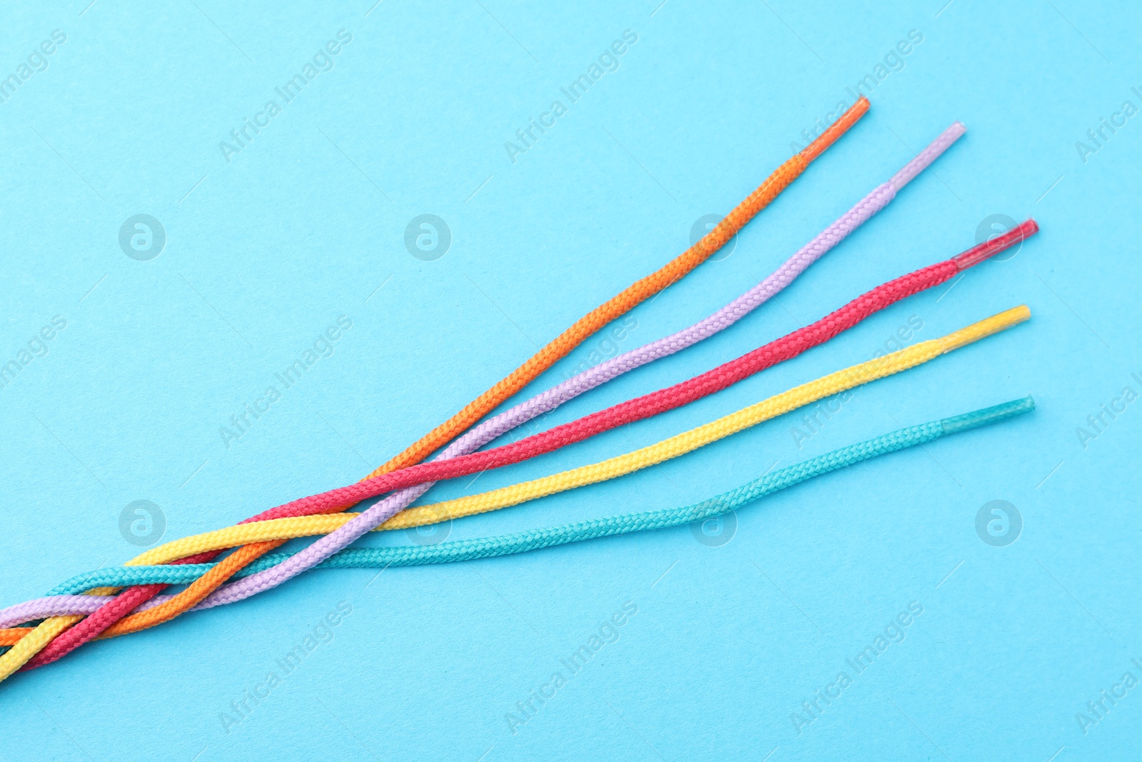 Photo of Braided colorful ropes on light blue background, top view. Unity concept