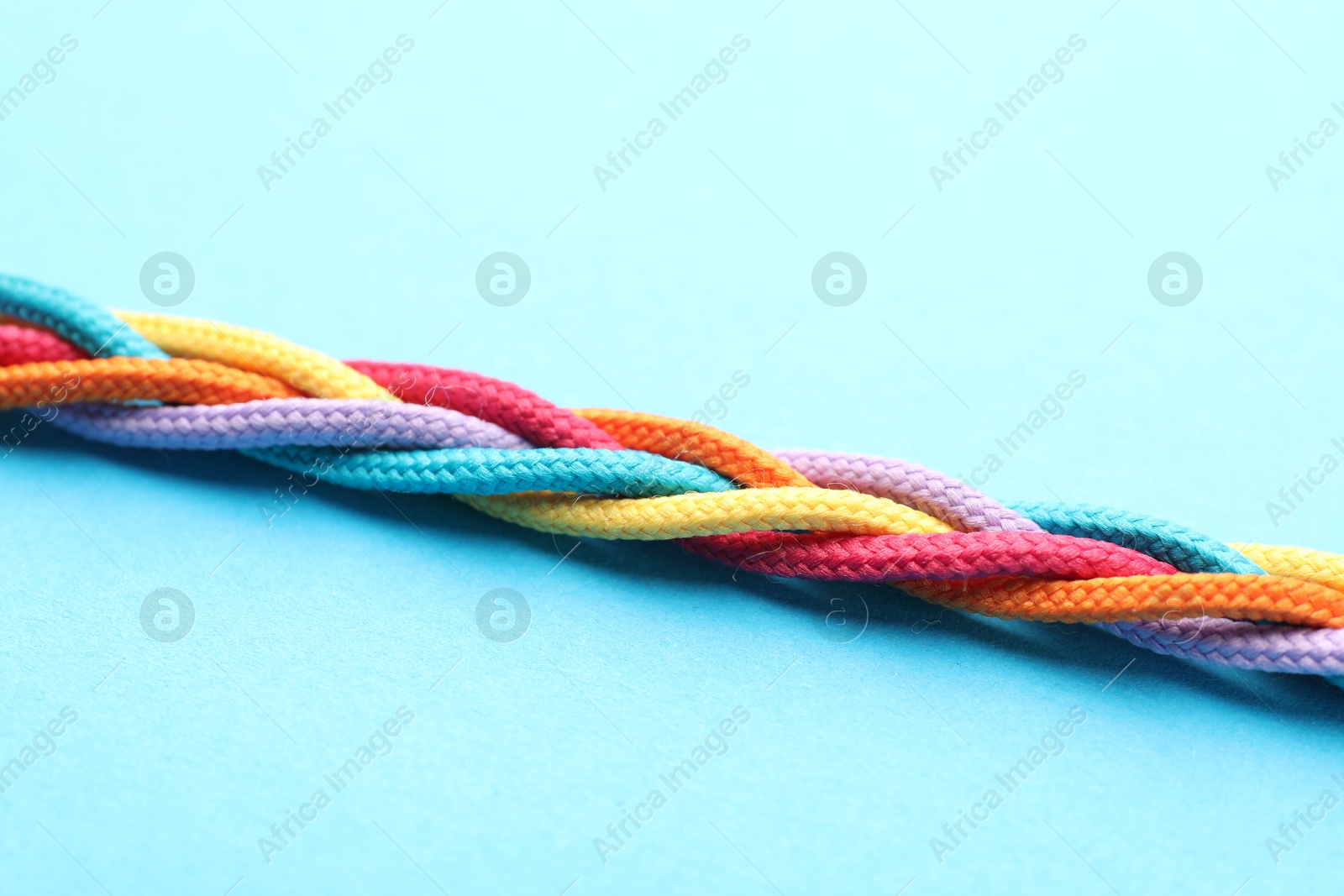 Photo of Braided colorful ropes on light blue background, closeup. Unity concept