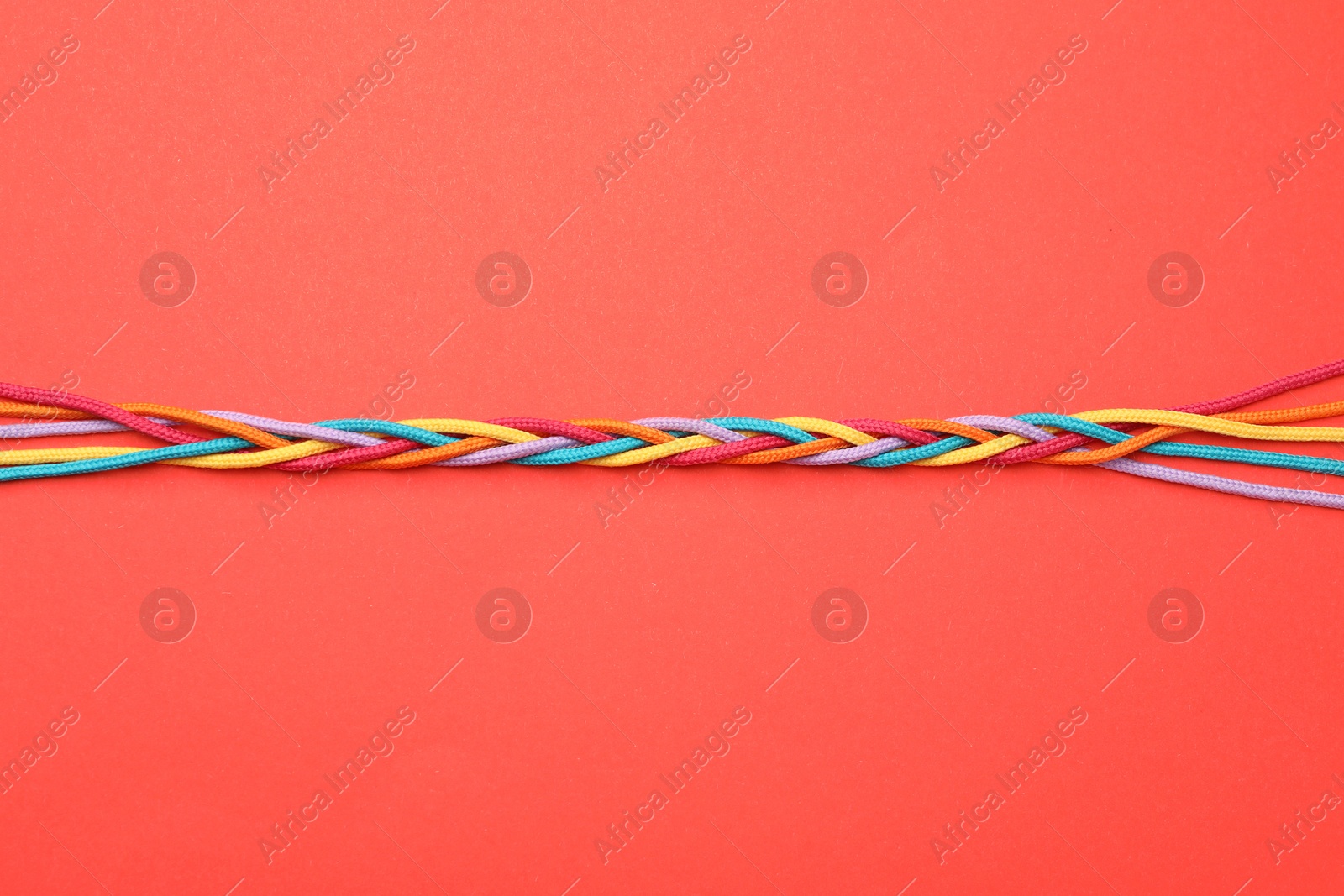 Photo of Braided colorful ropes on red background, top view. Unity concept