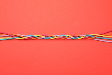 Photo of Braided colorful ropes on red background, top view. Unity concept