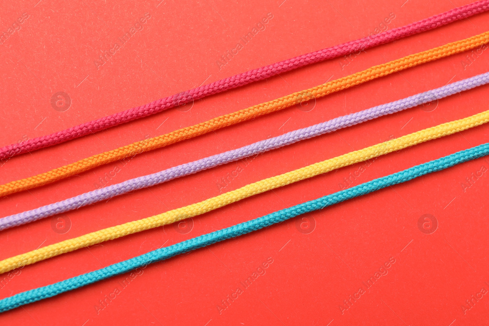 Photo of Colorful ropes on red background, top view. Unity concept