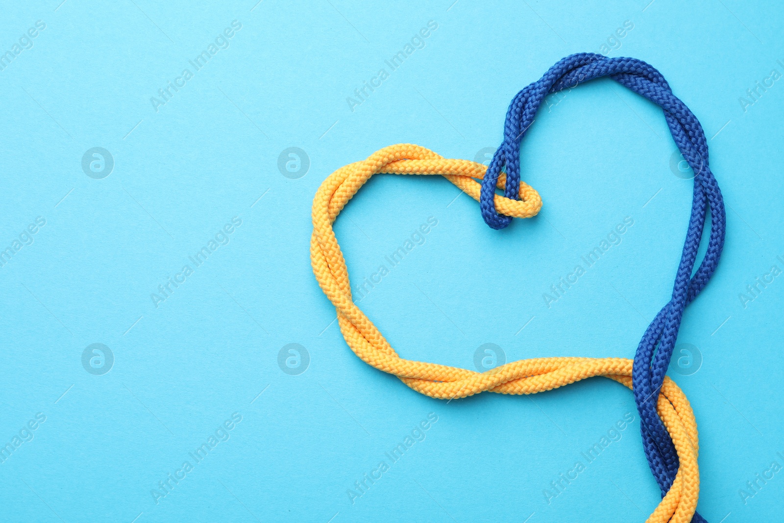 Photo of Heart made of tied ropes on light blue background, top view with space for text. Unity concept