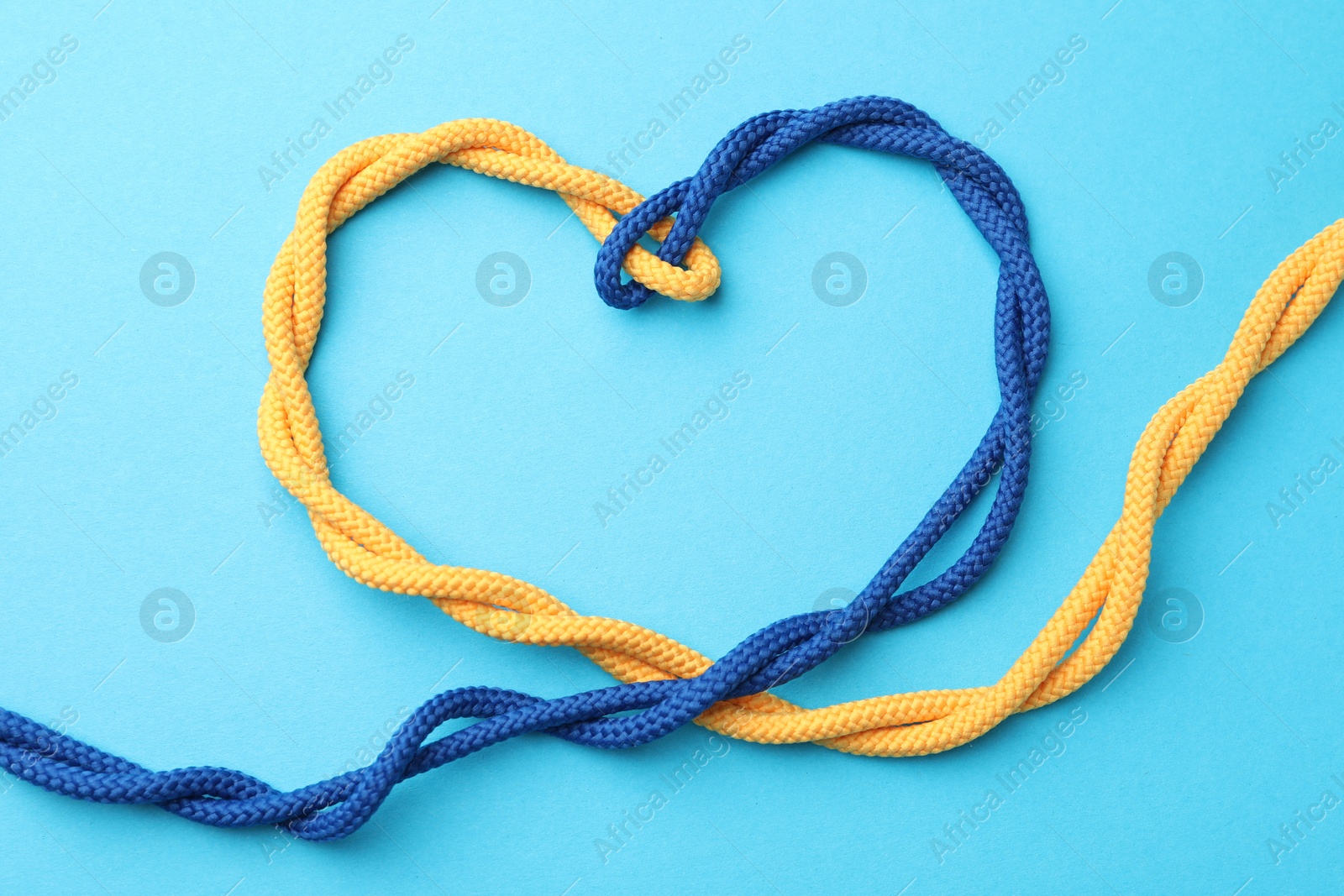 Photo of Heart made of tied ropes on light blue background, top view. Unity concept