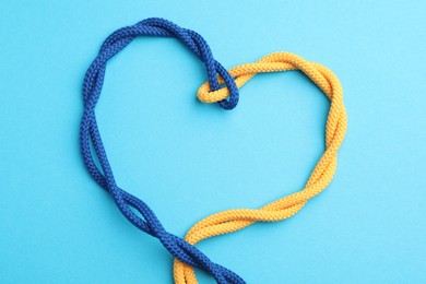 Photo of Heart made of tied ropes on light blue background, top view. Unity concept