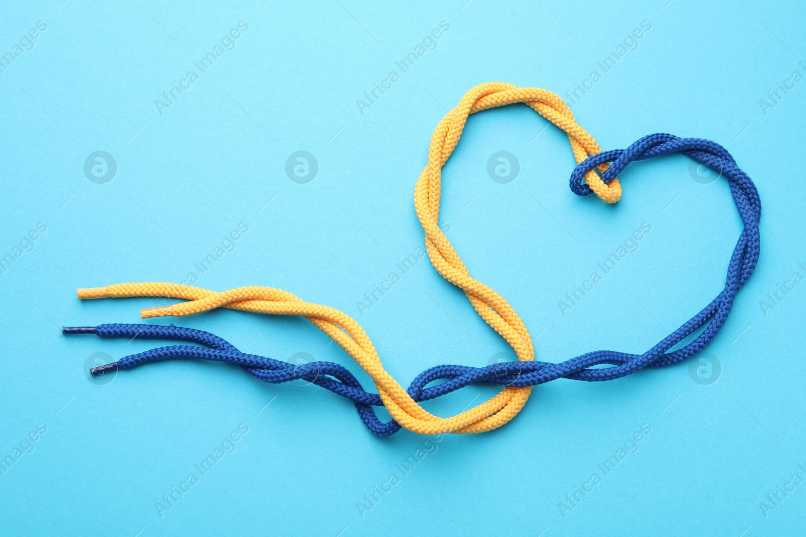 Photo of Heart made of tied ropes on light blue background, top view. Unity concept