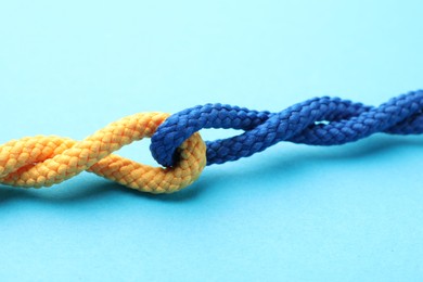 Photo of Colorful ropes tied together on light blue background, closeup. Unity concept