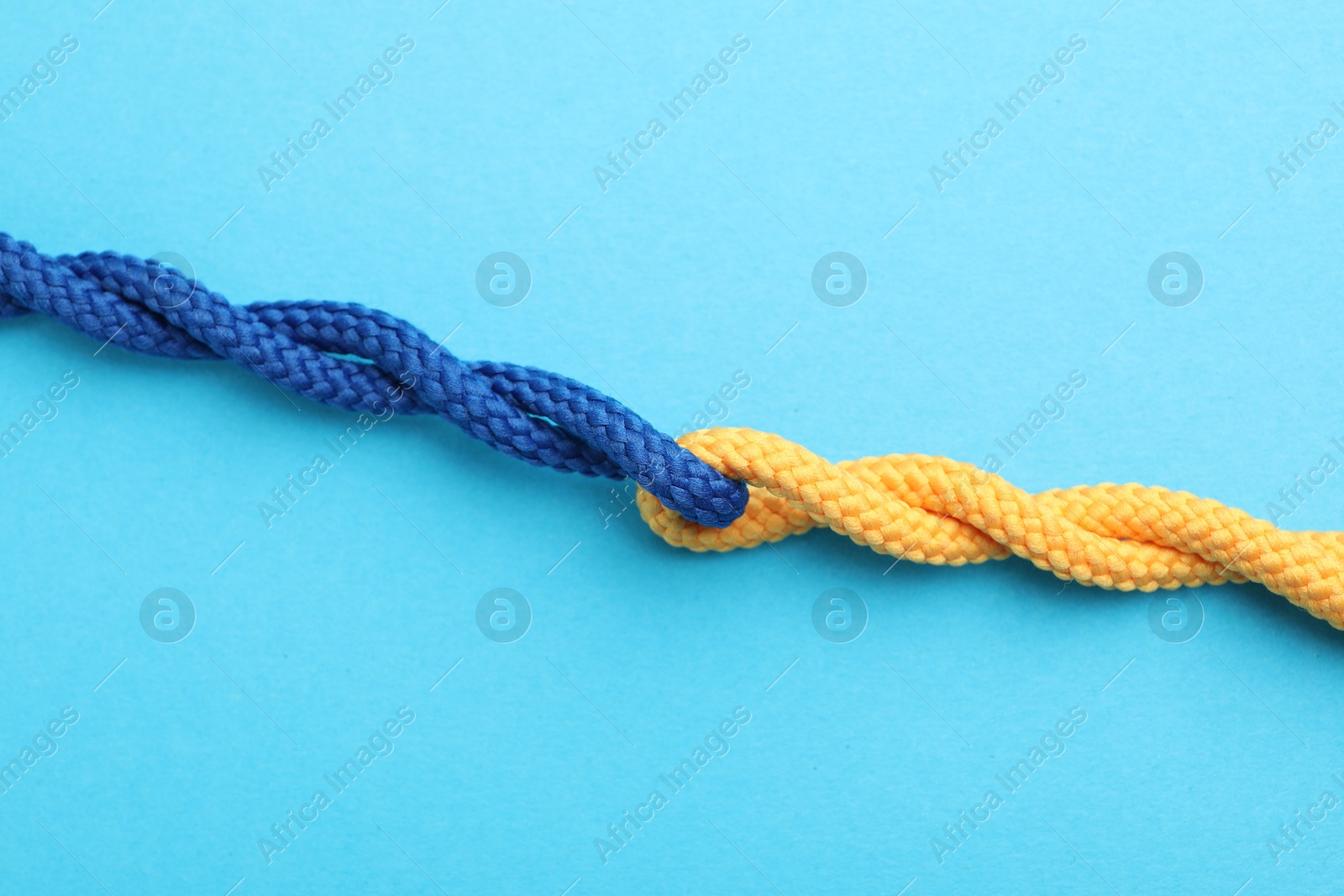 Photo of Colorful ropes tied together on light blue background, top view. Unity concept