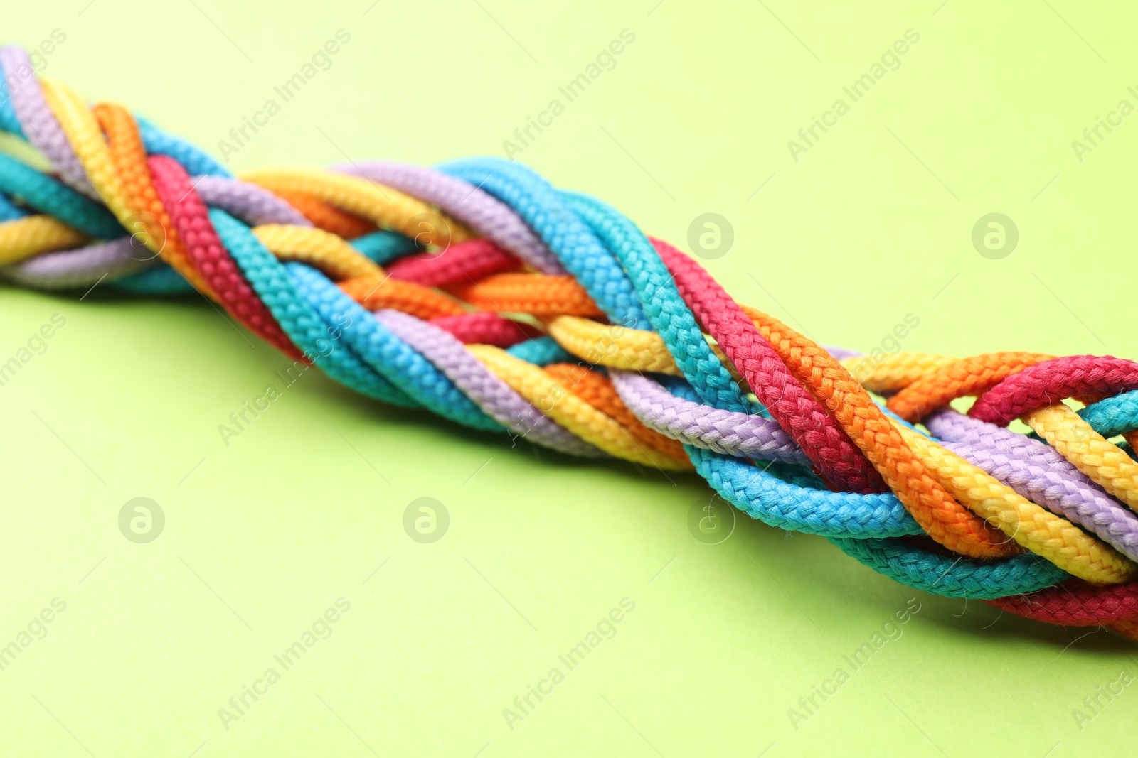 Photo of Braided colorful ropes on light green background, closeup. Unity concept