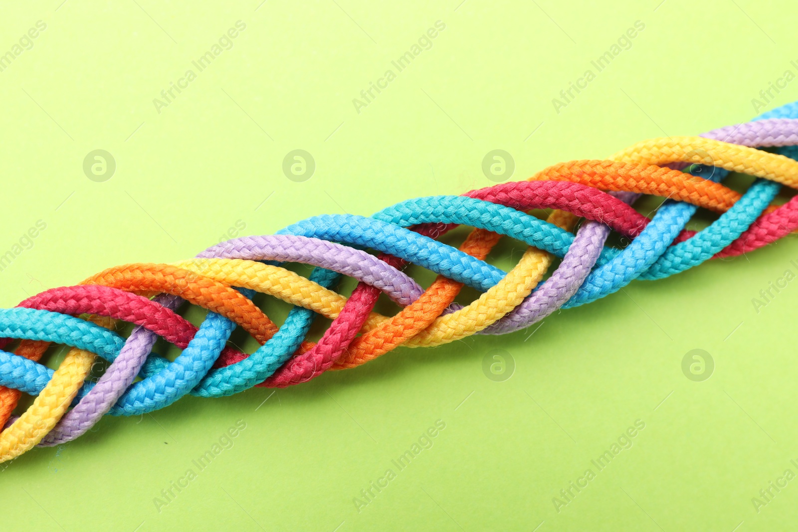 Photo of Braided colorful ropes on light green background, top view. Unity concept