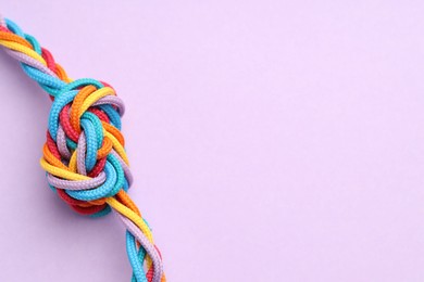 Photo of Colorful ropes tied in knot on lilac background, closeup with space for text. Unity concept