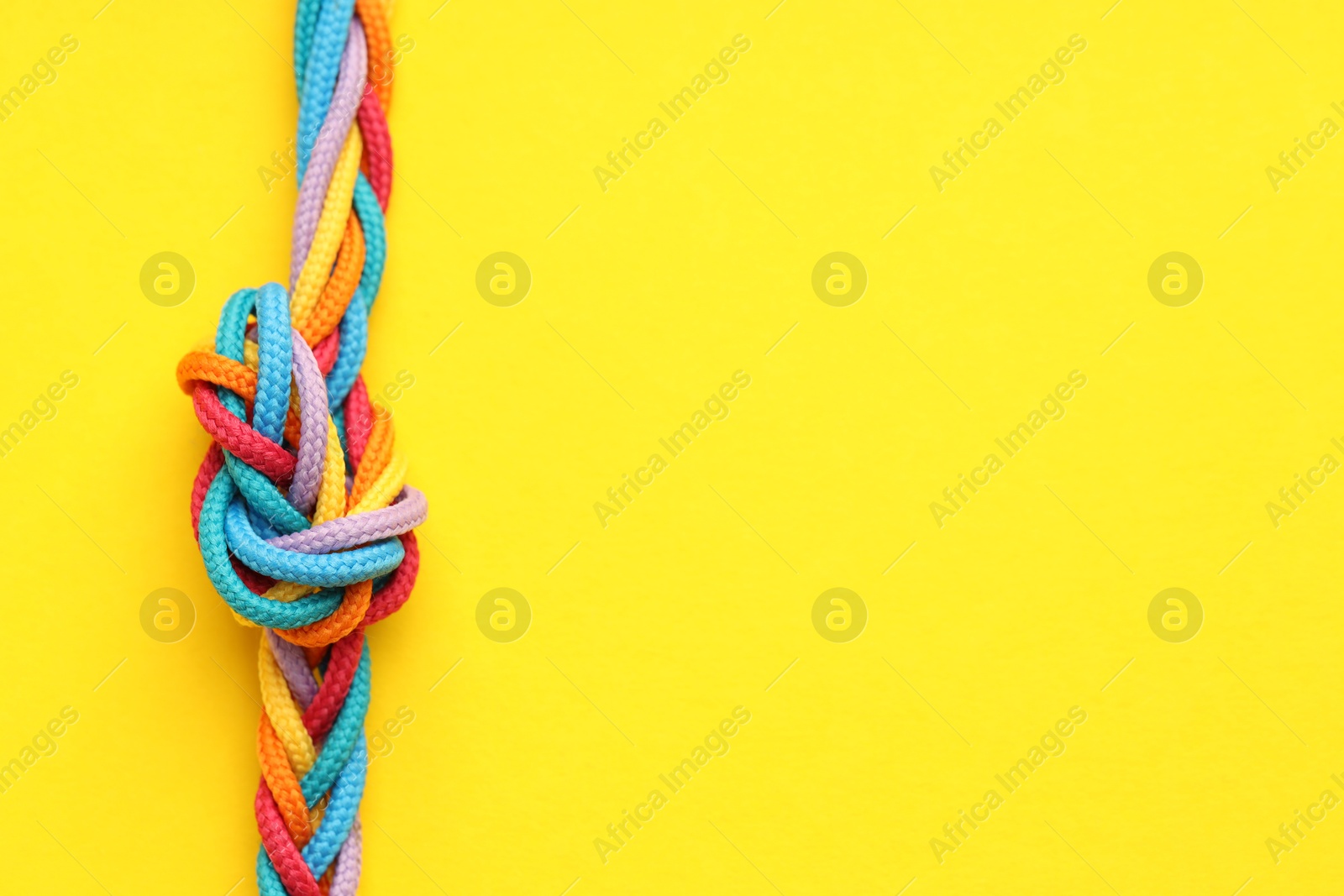 Photo of Colorful ropes tied in knot on yellow background, top view with space for text. Unity concept