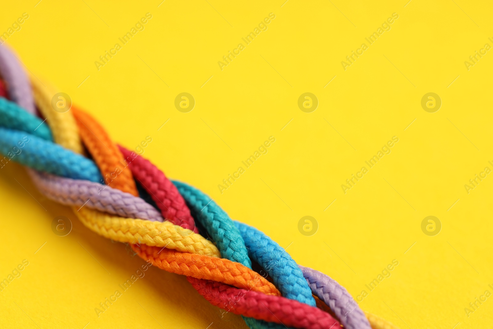 Photo of Braided colorful ropes on yellow background, closeup with space for text. Unity concept