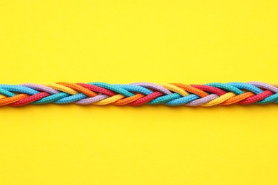 Photo of Braided colorful ropes on yellow background, top view. Unity concept