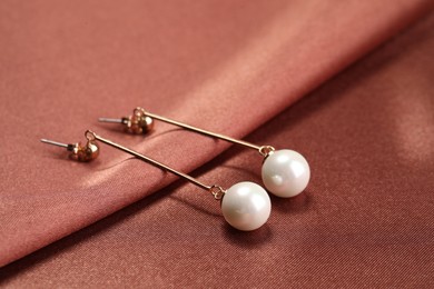 Photo of Beautiful pearl earrings on brown silk, closeup