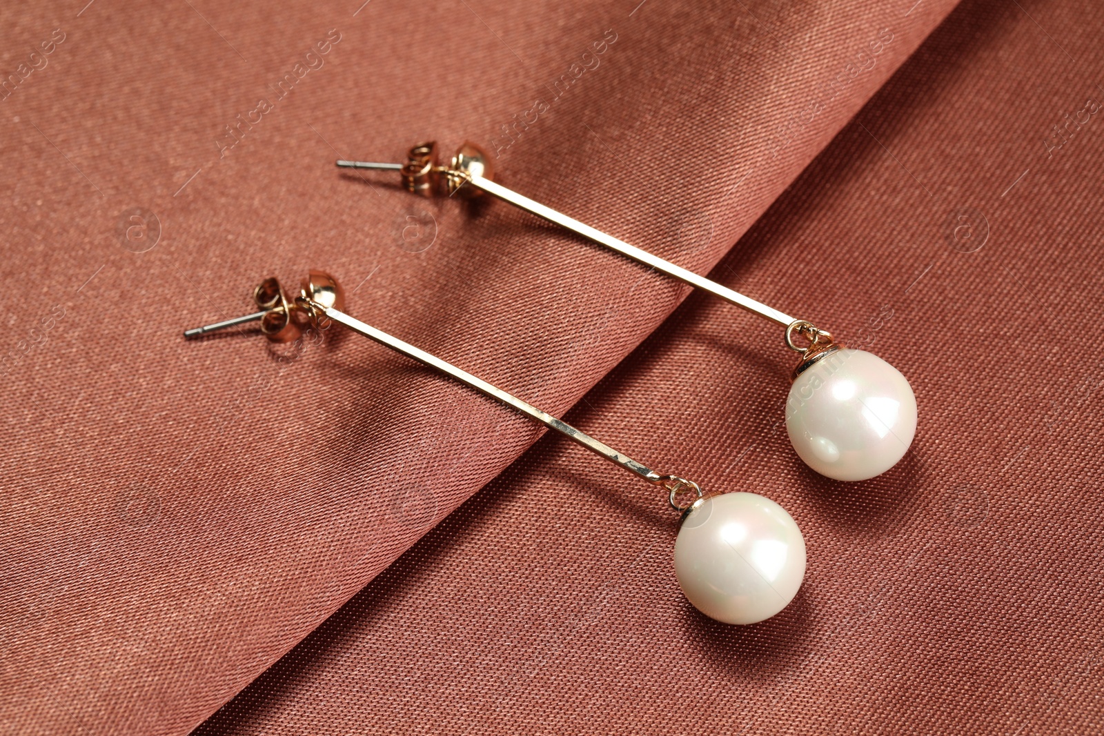 Photo of Beautiful pearl earrings on brown silk, closeup