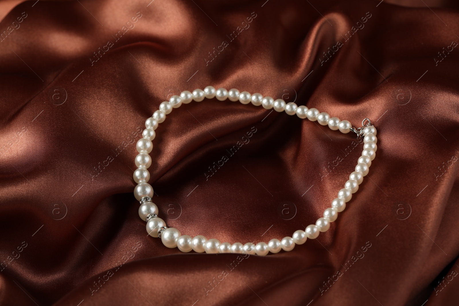 Photo of Beautiful pearl necklace on brown silky fabric