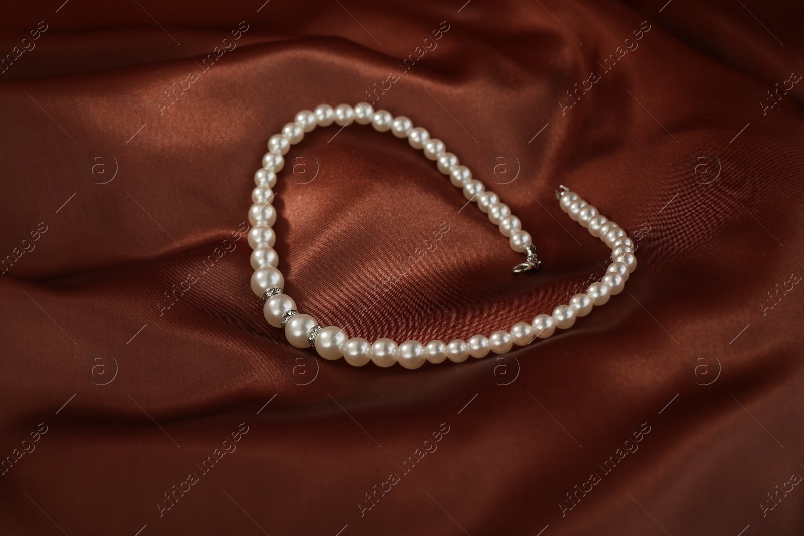 Photo of Beautiful pearl necklace on brown silk, closeup