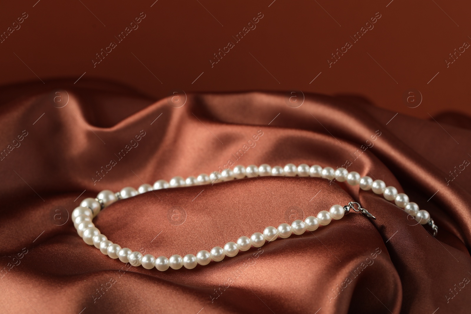 Photo of Beautiful pearl necklace on brown silk, closeup