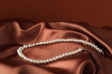 Photo of Beautiful pearl necklace on brown silk, closeup