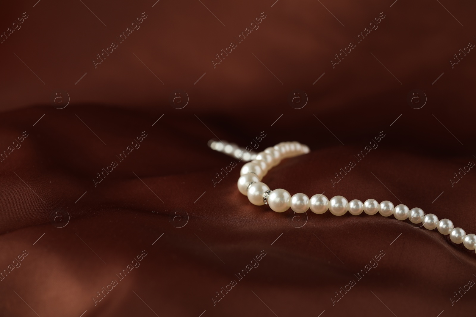 Photo of Beautiful pearl necklace on brown silk, closeup. Space for text