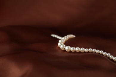 Photo of Beautiful pearl necklace on brown silk, closeup. Space for text