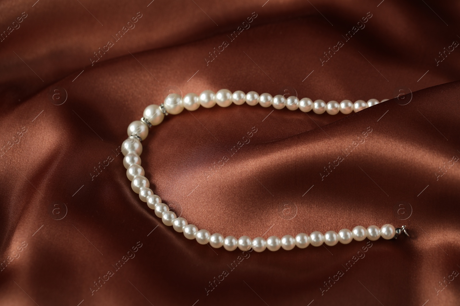 Photo of Beautiful pearl necklace on brown silk, closeup