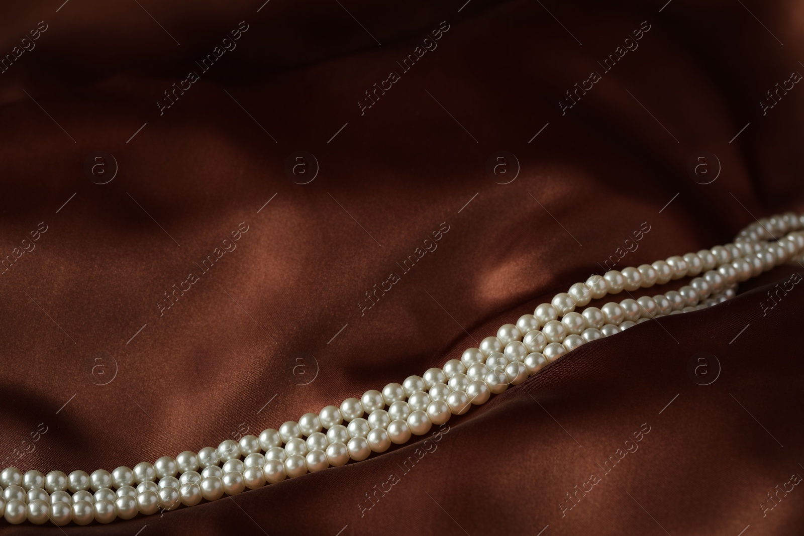 Photo of Beautiful pearl necklace on brown silk, closeup. Space for text