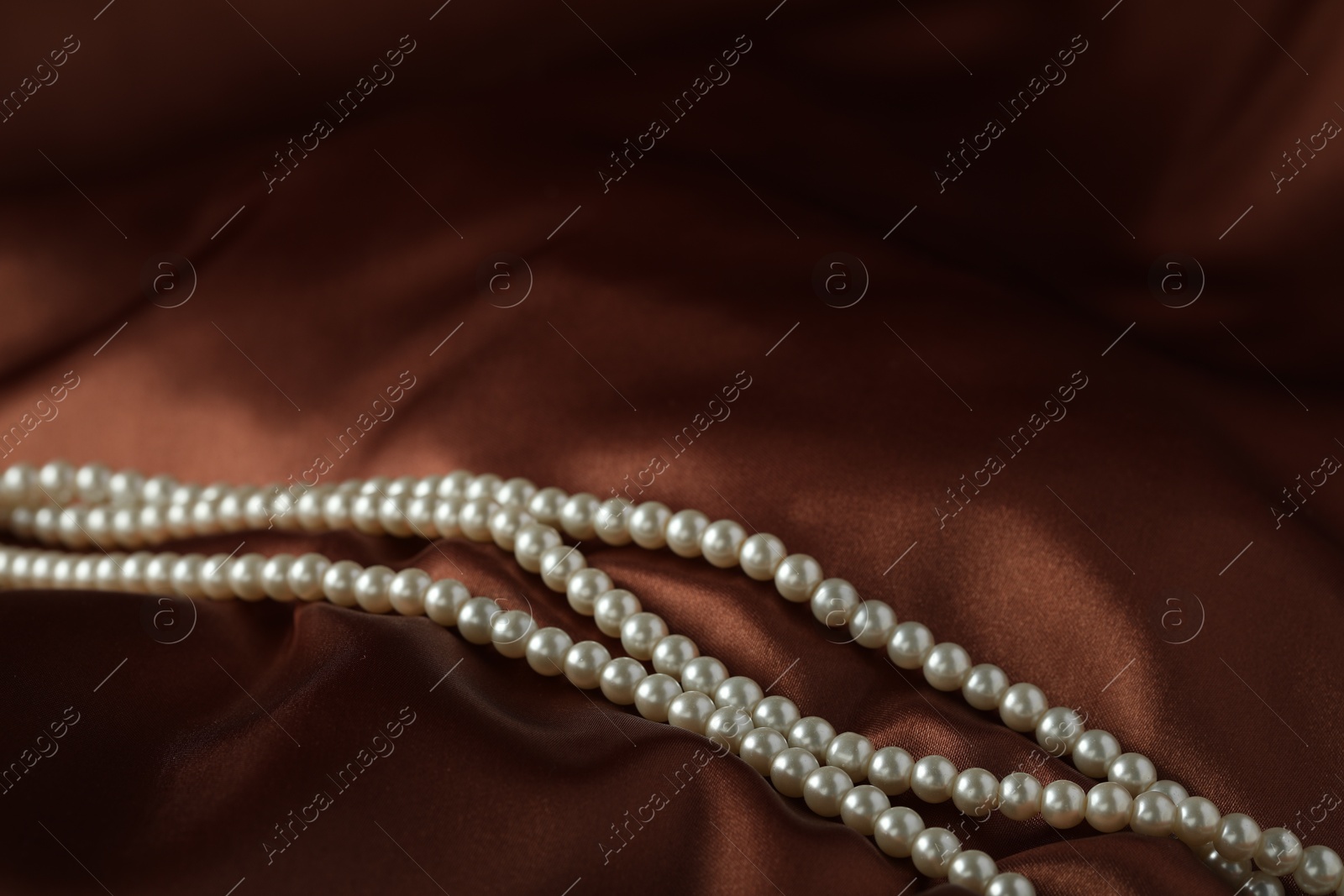 Photo of Beautiful pearl necklace on brown silk, closeup