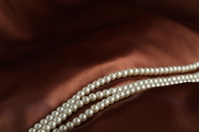 Photo of Beautiful pearl necklace on brown silk, closeup