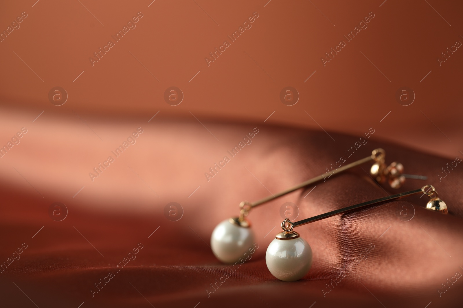 Photo of Beautiful pearl earrings on brown silk, closeup. Space for text