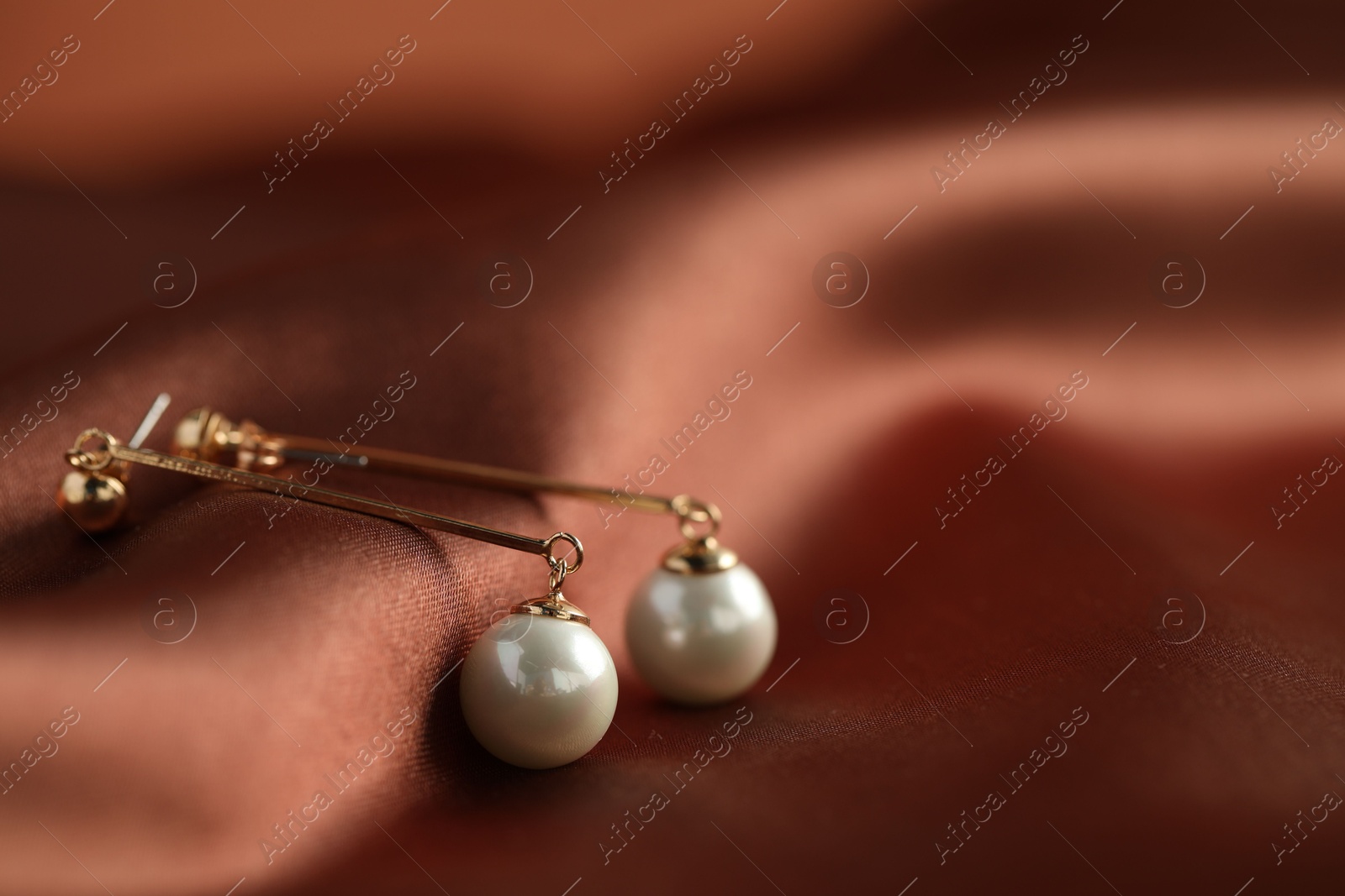 Photo of Beautiful pearl earrings on brown silk, closeup. Space for text