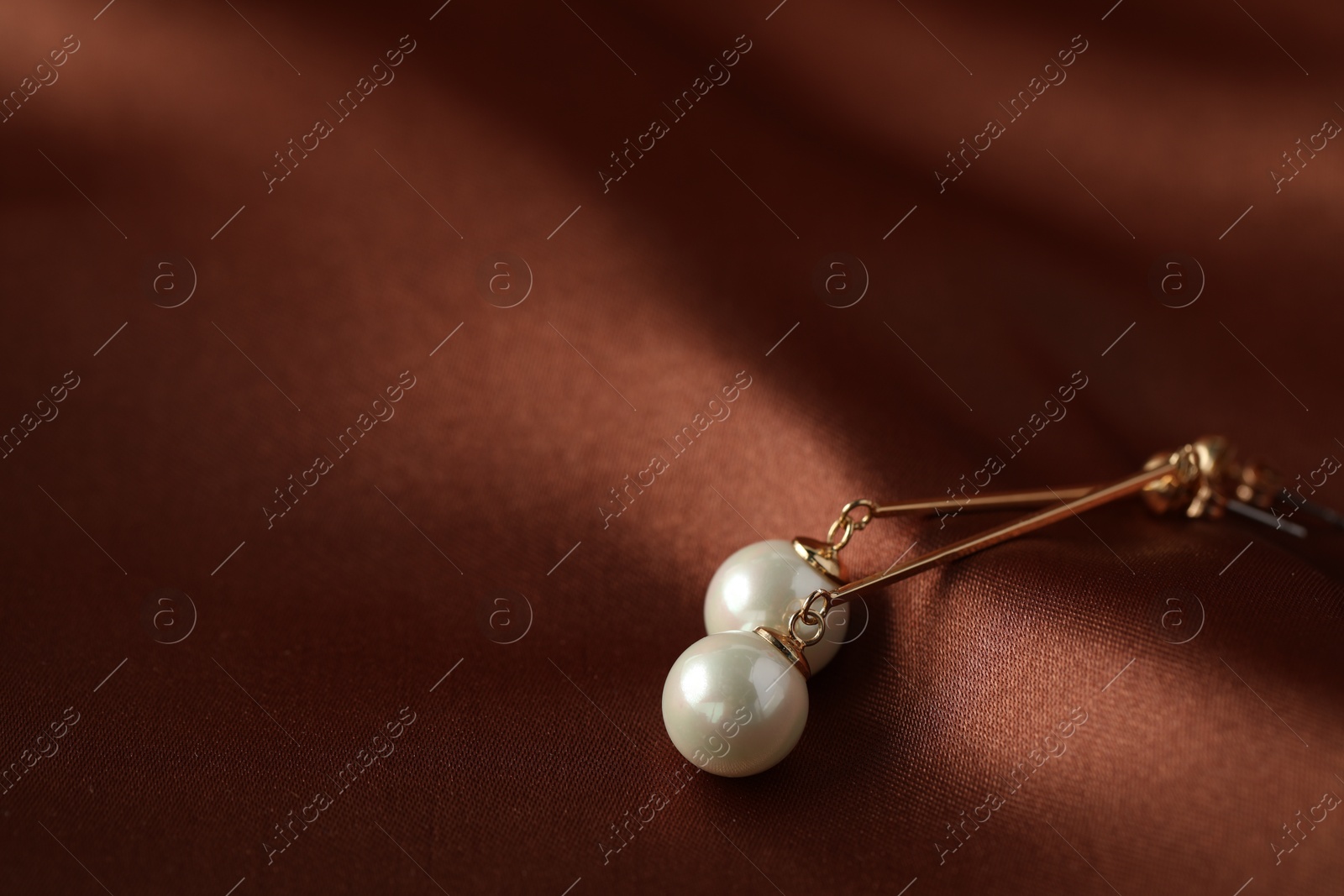 Photo of Beautiful pearl earrings on brown silk, closeup. Space for text